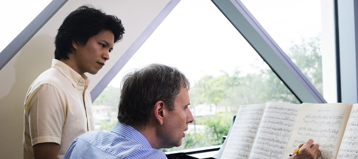 Instructor making notations on sheet music while a student musician looks on