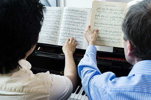 Two people examine sheet music resting on a piano
