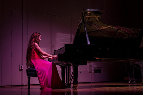 Woman in a red dress plays the piano on stage during a performance