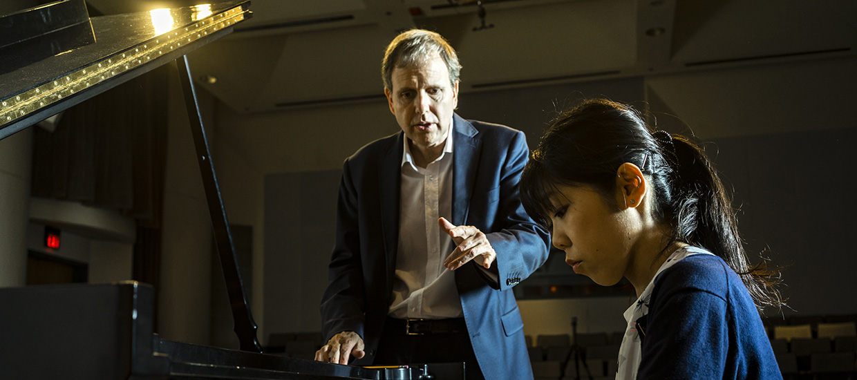 A woman pianist receiving instruction from a man in a suit