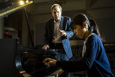 A woman pianist receiving instruction from a man in a suit
