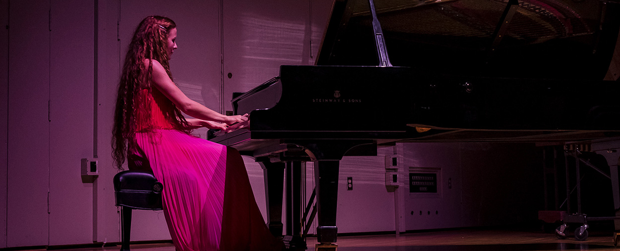 Woman in a red dress plays the piano on stage during a performance